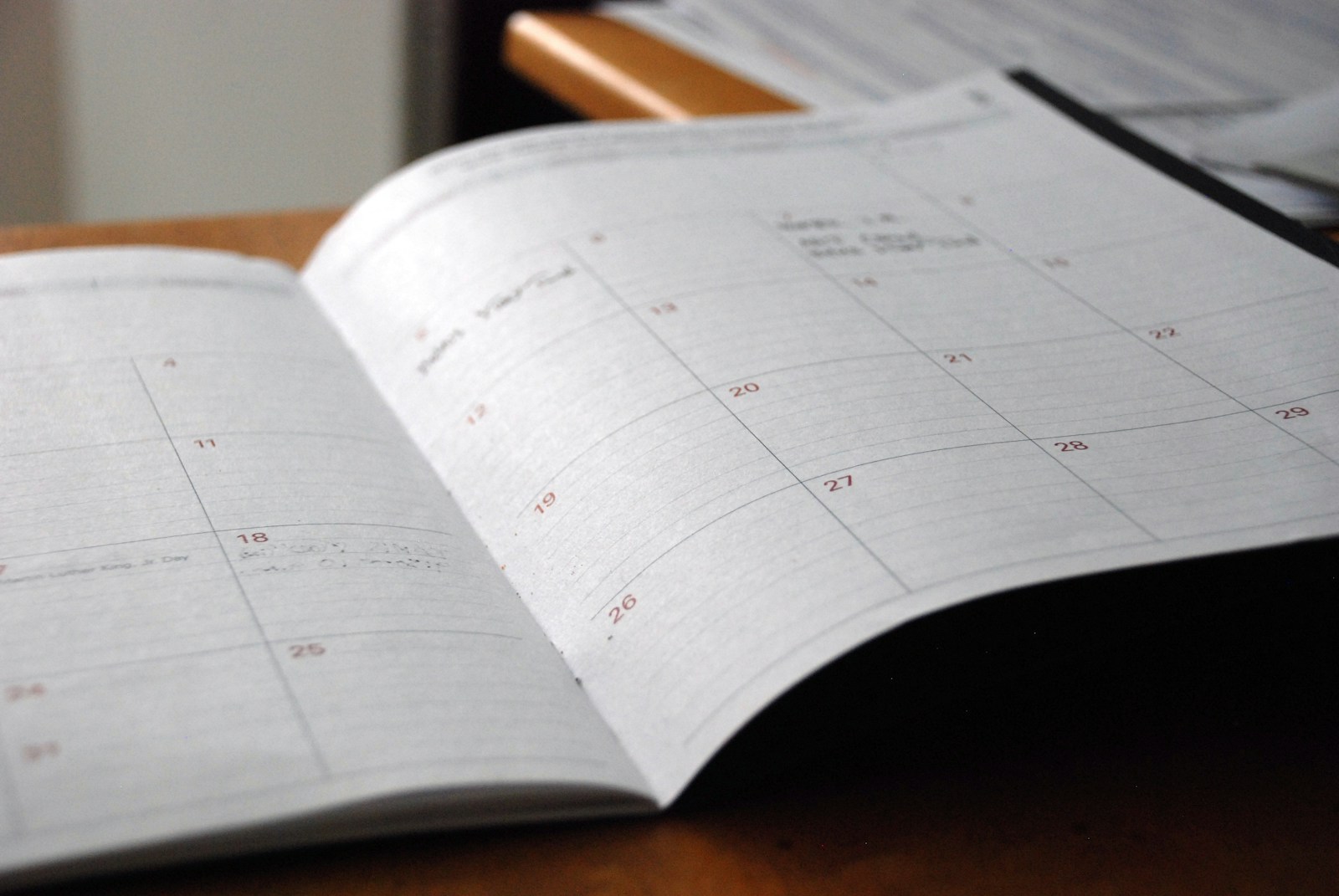An open paper monthly planner lying on a wooden desk with a few handwritten appointments in its date boxes