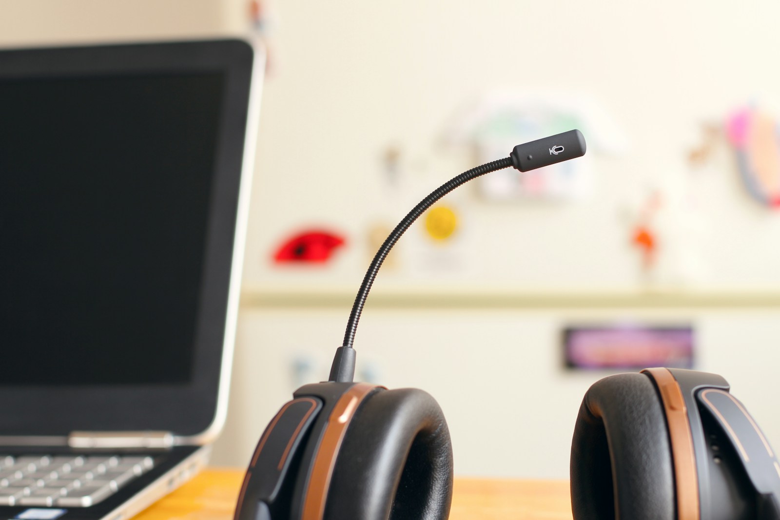A black headset with a boom microphone resting on a wooden desk beside an open laptop