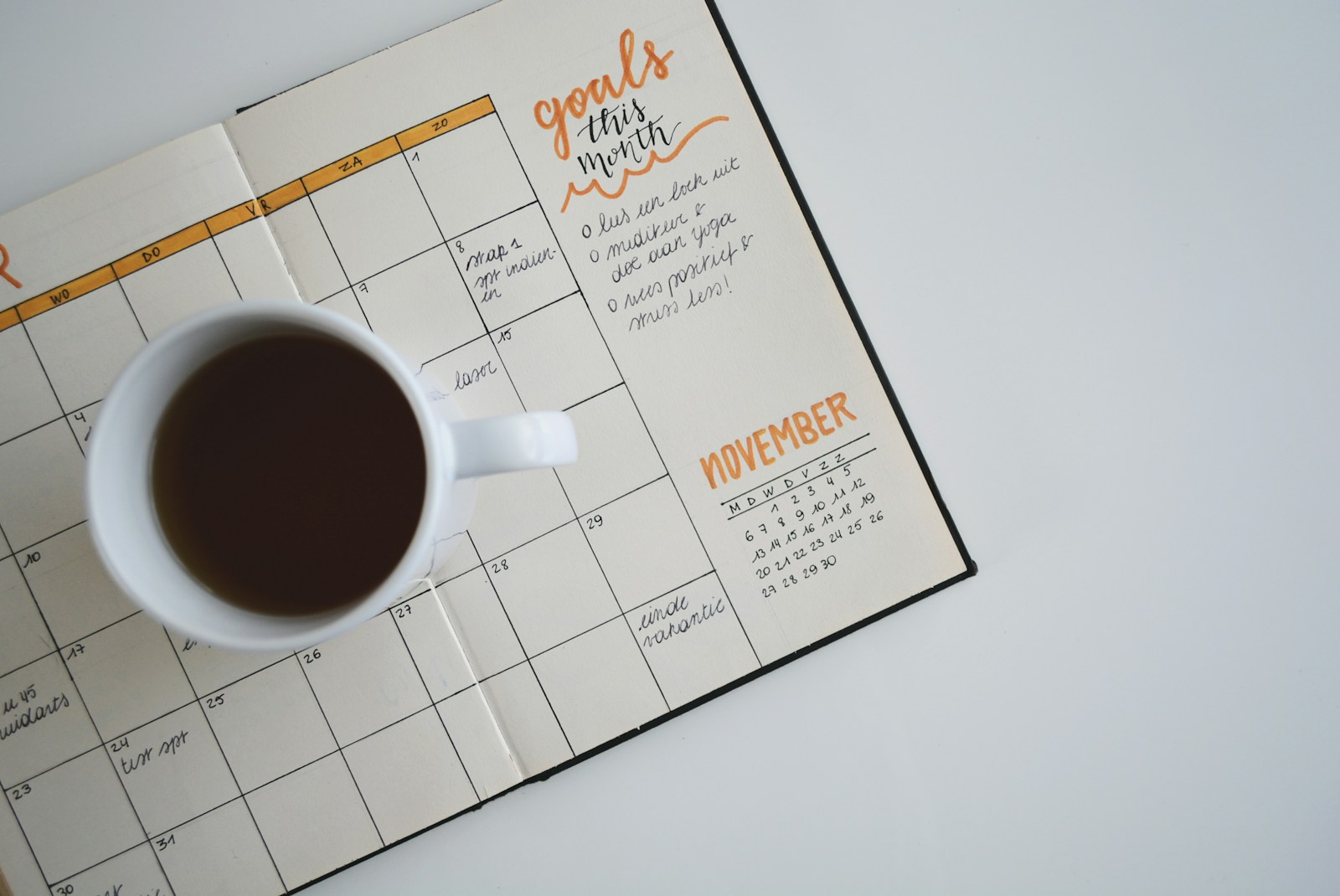 A cup of coffee resting on an open monthly planner with handwritten goals and dated boxes
