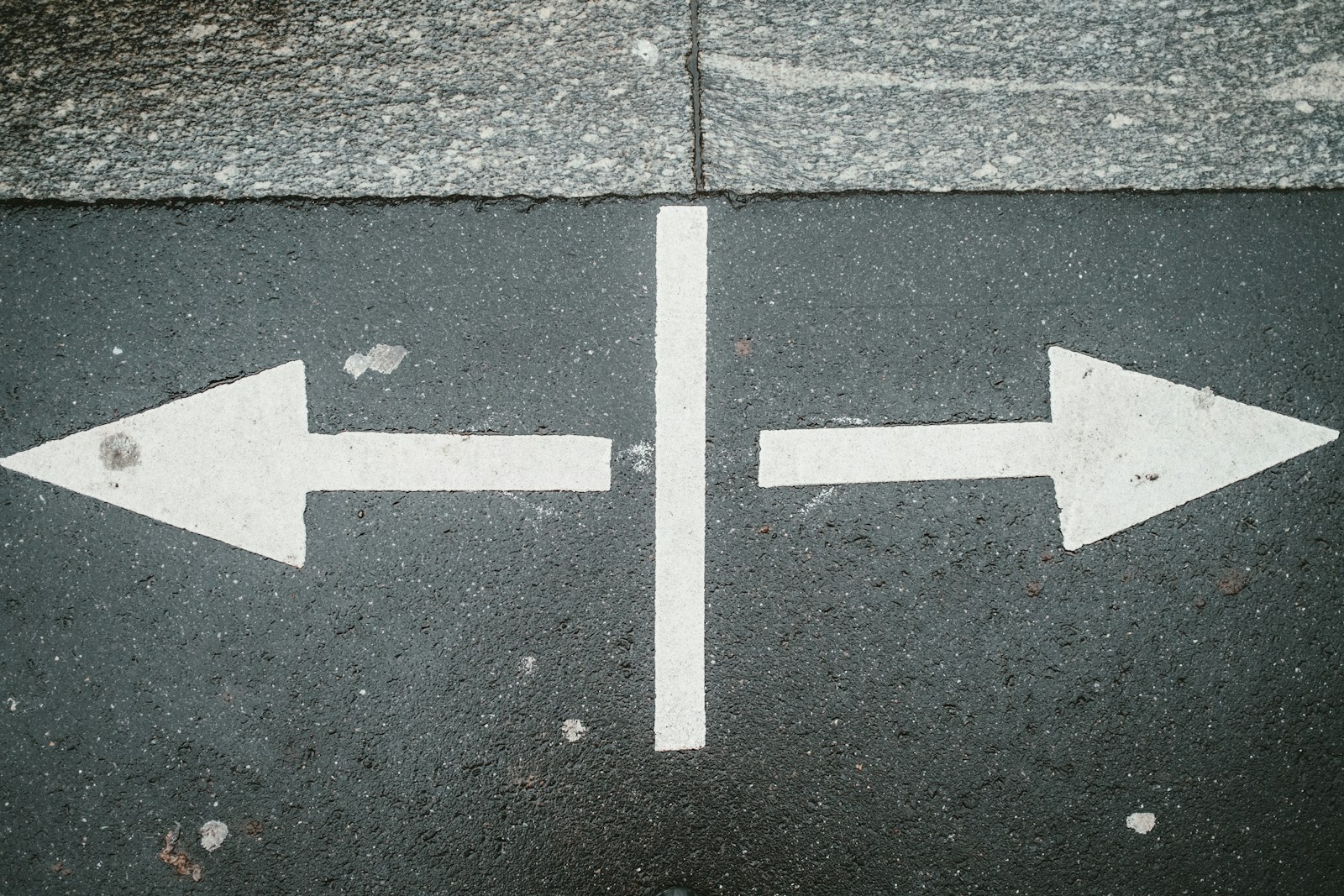 Two white arrows painted on dark asphalt pointing in opposite directions, separated by a white line