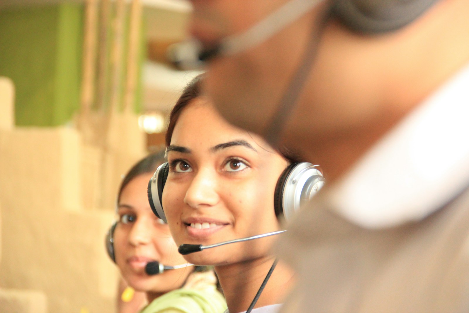 Two women wearing headsets with microphones at a support desk, one smiling toward the camera